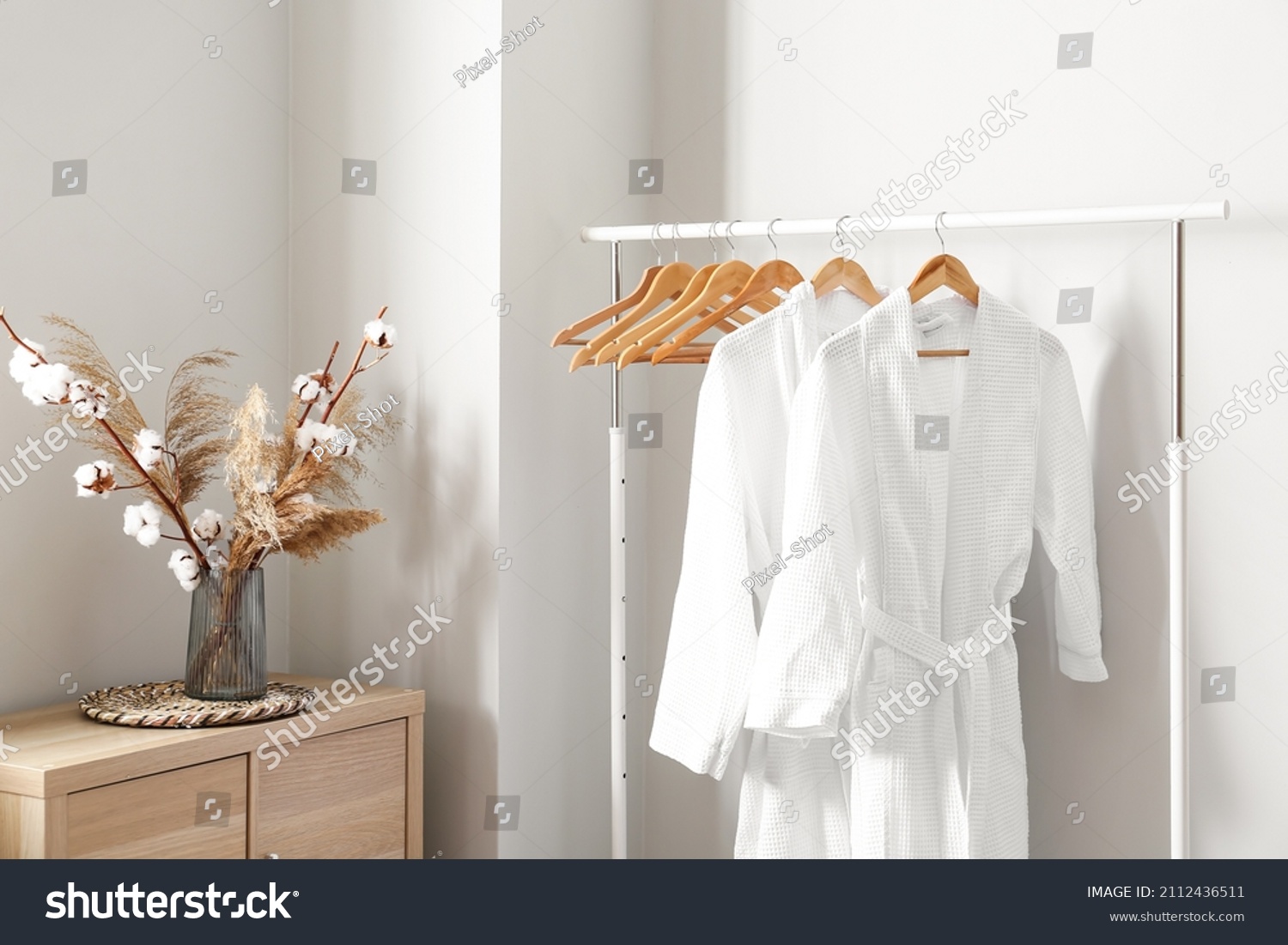 Rack with white bathrobes near light wall in room #2112436511