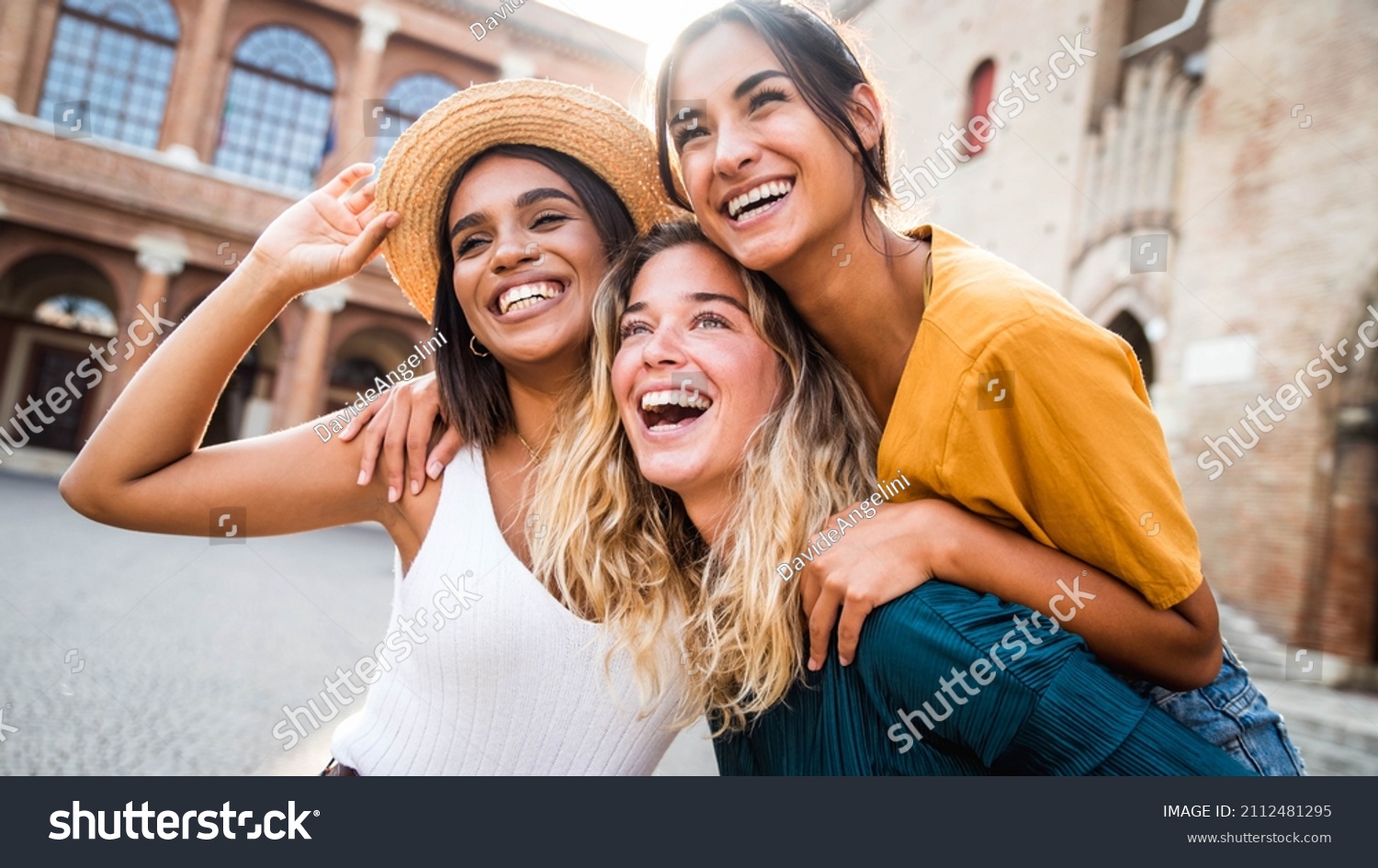 Three young multiracial women having fun on city street outdoors - Mixed race female friends enjoying a holiday day out together - Happy lifestyle, youth and young females concept #2112481295