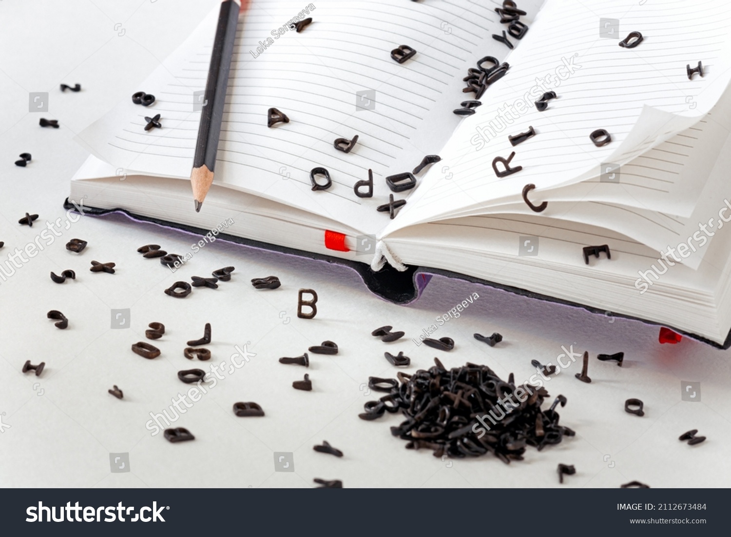 a lot of small black Latin letters scattered across the pages of a notebook and a table, the concept of grammar and spelling, creativity and ideas for a story #2112673484