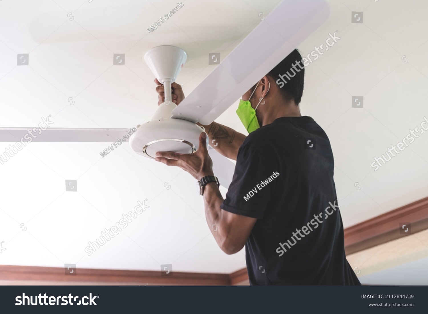 A handyman installs a ceiling fan, tightening the screws of the fan blades. At the living room. Home renovation or construction. #2112844739