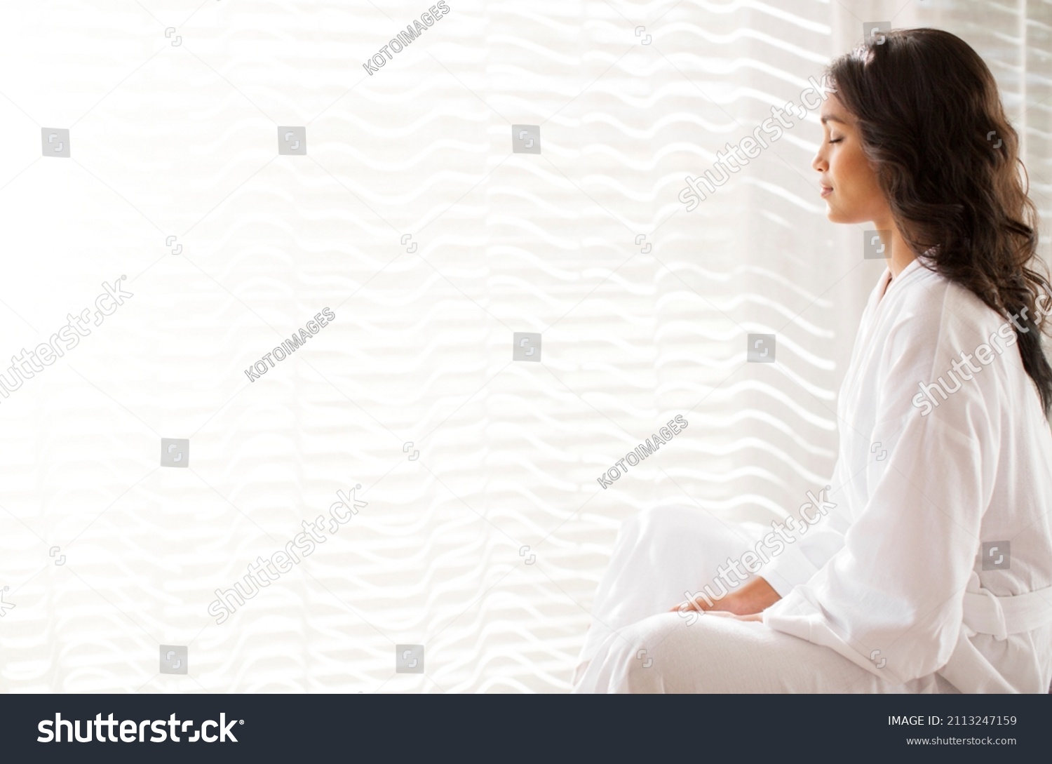 Serene woman in bathrobe meditating at sunny window #2113247159