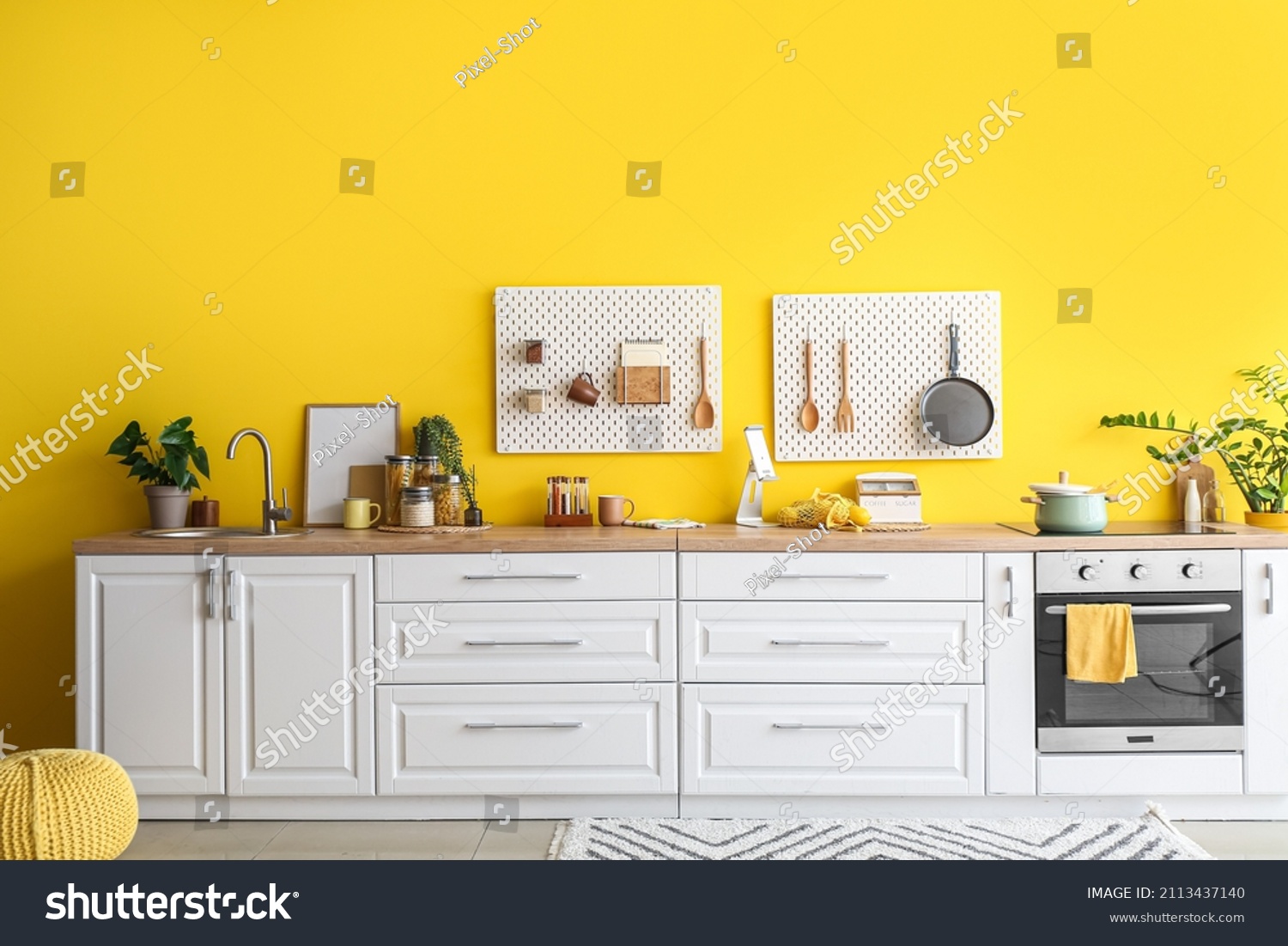 Interior of stylish kitchen with white counters, peg boards and yellow wall #2113437140