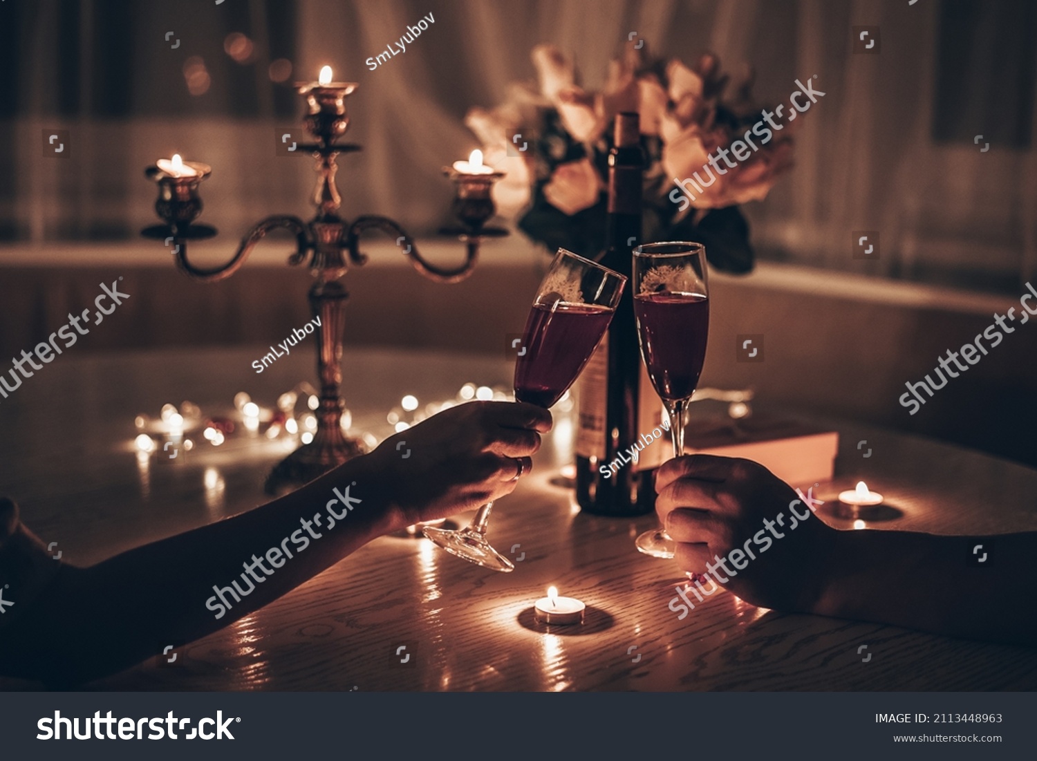 Hands man and woman holding glasses of wine having romantic candlelight dinner at table at home. Hands man and woman holding glass of wine. Concept of Valentine's day or Candlelight date at night. #2113448963