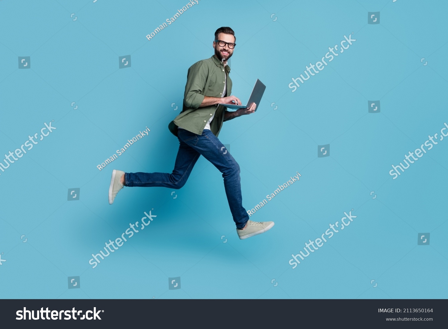 Profile photo of sporty active guy jump hold netbook run work wear specs green shirt isolated blue color background #2113650164