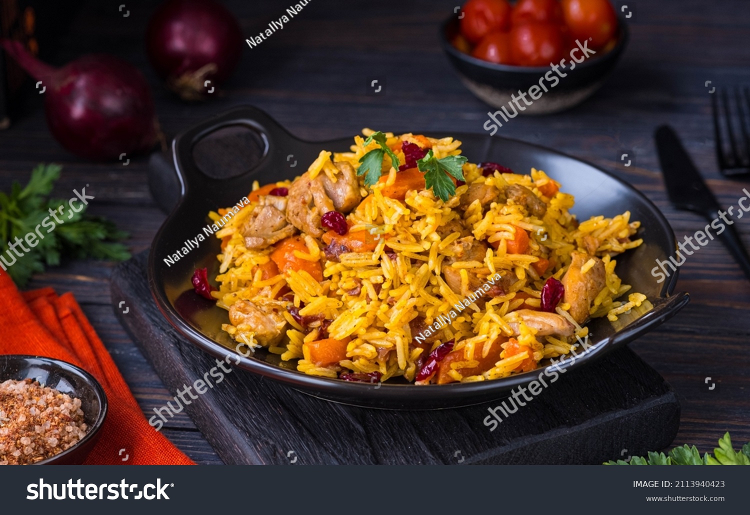 Pilaf, a dish of rice, chicken, carrots with spices and dried cranberries on a black plate on a dark wooden background. Eastern cuisine. #2113940423
