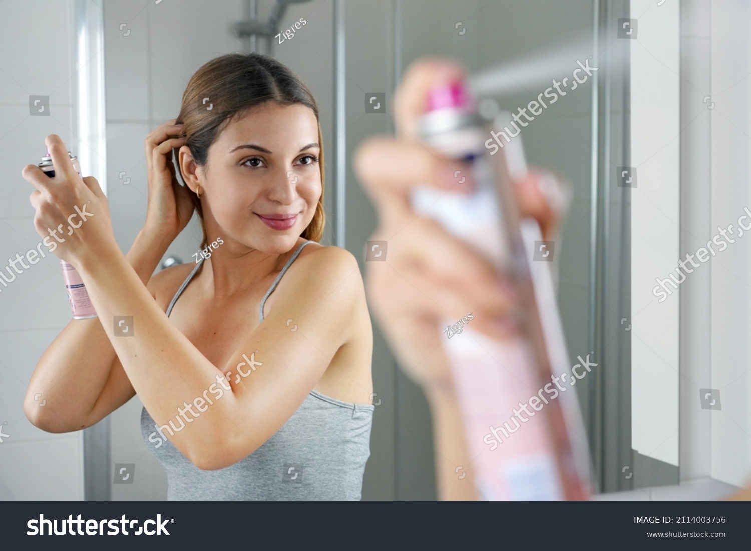 Young woman applying dry shampoo on her hair before going out. Fast and easy way to covering grey hair with instant spray dye. #2114003756