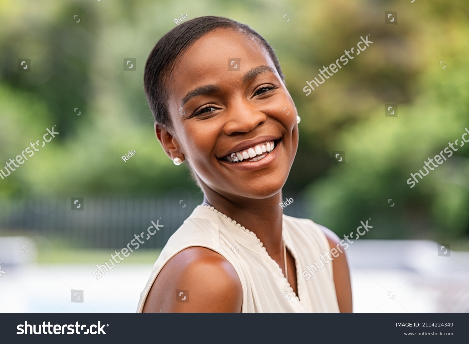 Portrait of smiling middle aged african woman looking at camera. Cheerful black mid adult woman smiling outdoor. Close up face of beautiful black lady laughing at park. #2114224349