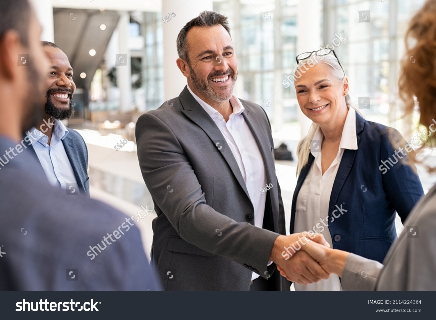 Happy mature businessman shaking hands with businesswoman in modern office. Successful entrepreneur greeting business woman with handshake. Agreement and business deal concept. #2114224364