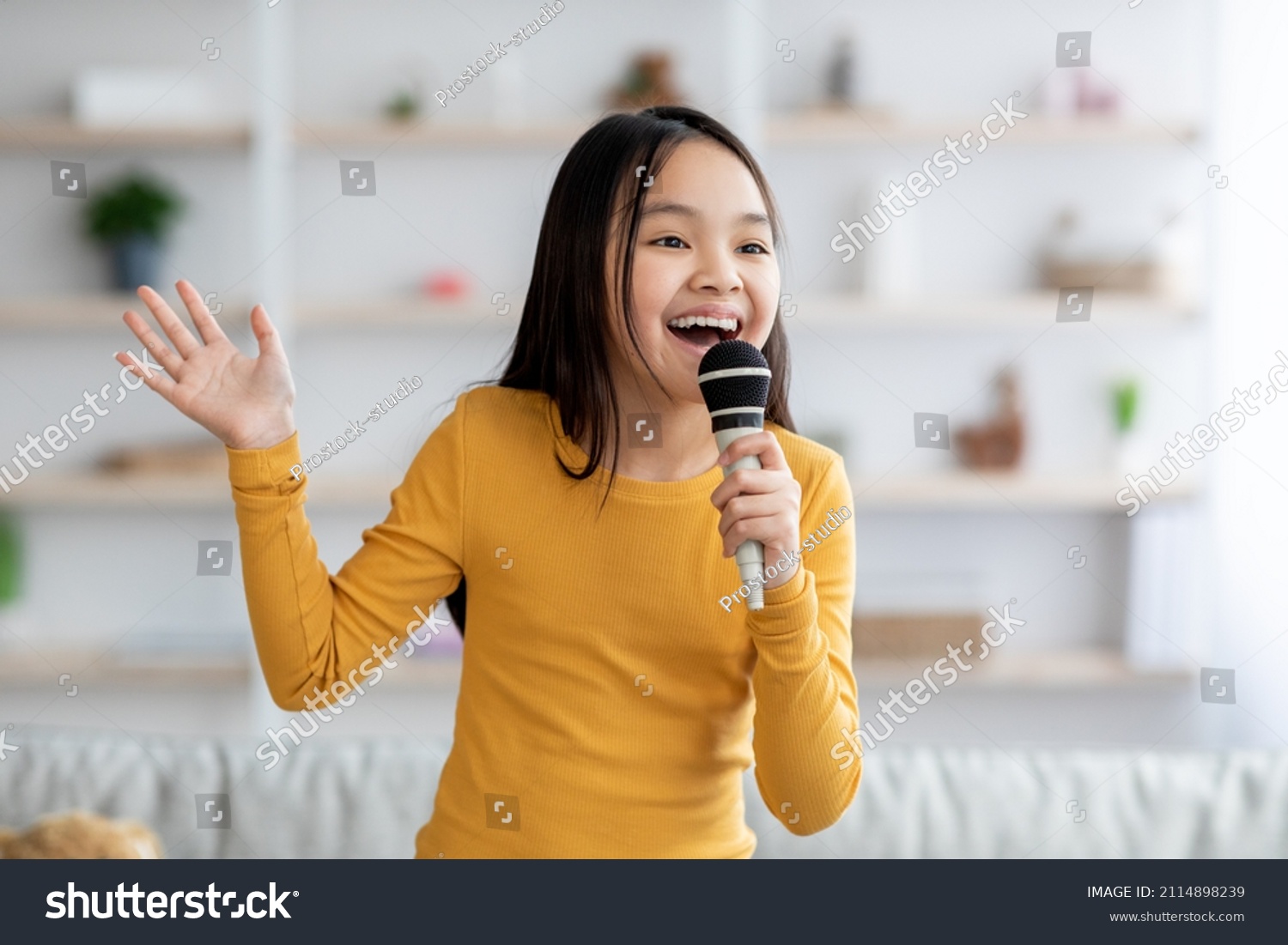 Portrait of cute pretty long-haired korean girl teenager singing at home, using microphone and gesturing, looking at copy space. Child singing karaoke, domestic entertainment for kids concept #2114898239