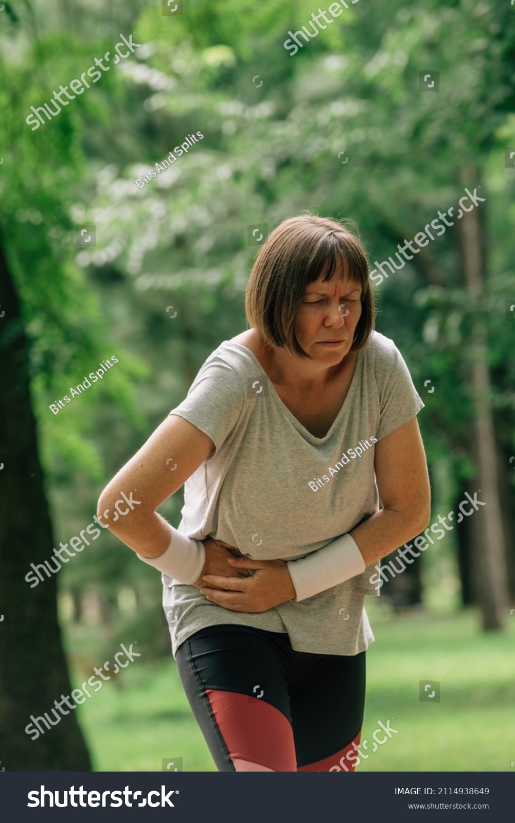 Female jogger with painful face grimace after feeling pain in lower abdomen during running in park #2114938649