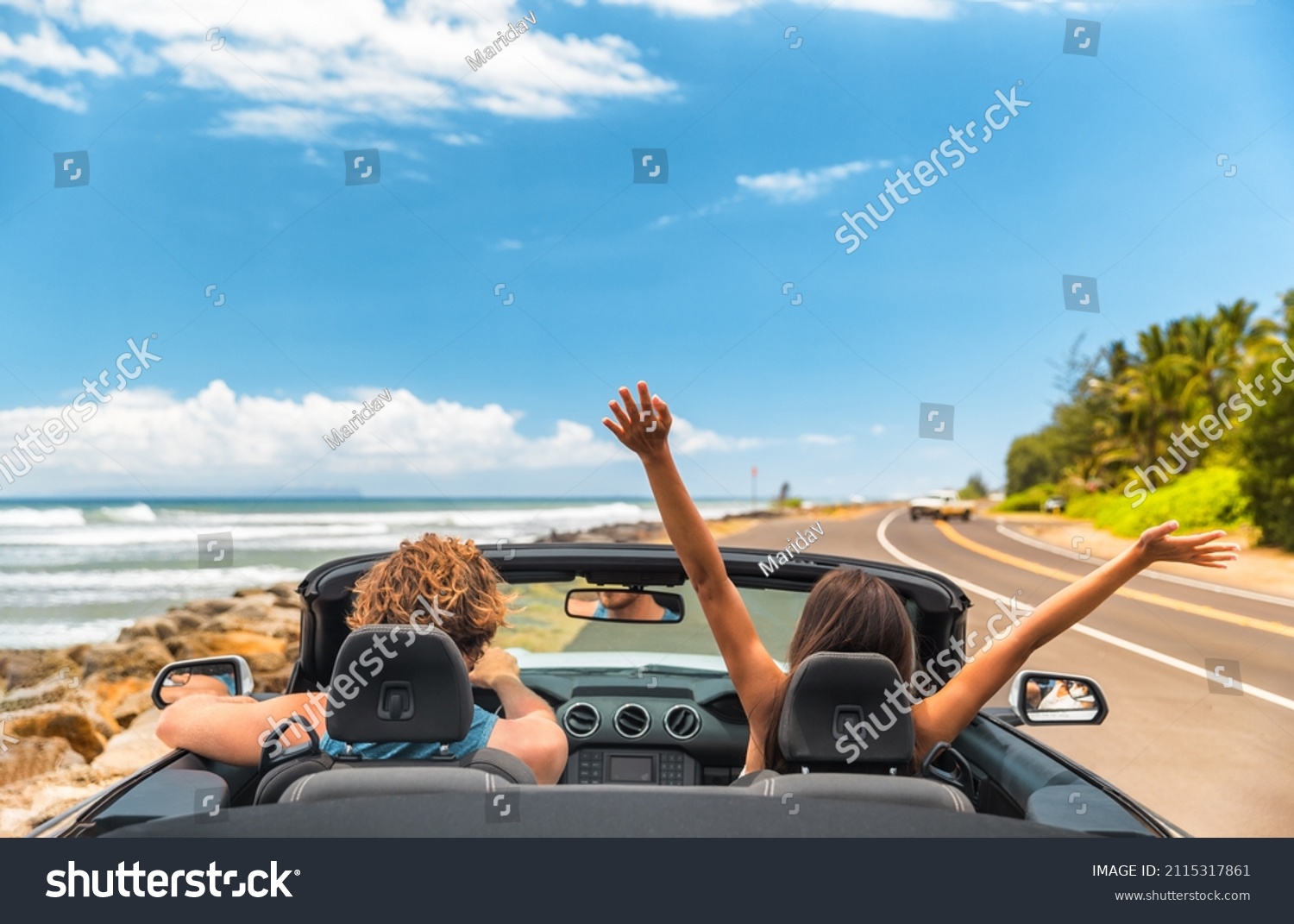 Road trip car holiday happy couple driving convertible car on summer travel Hawaii vacation. Woman with arms up having fun, young man driver #2115317861