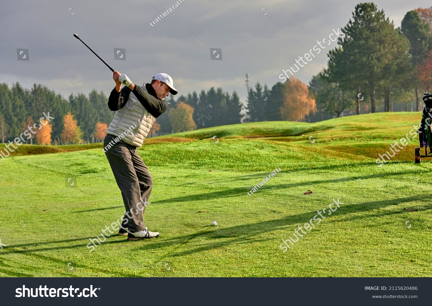 Golfer on a golf course in winter with wet grass, hitting the ball with a golf club. #2115620486
