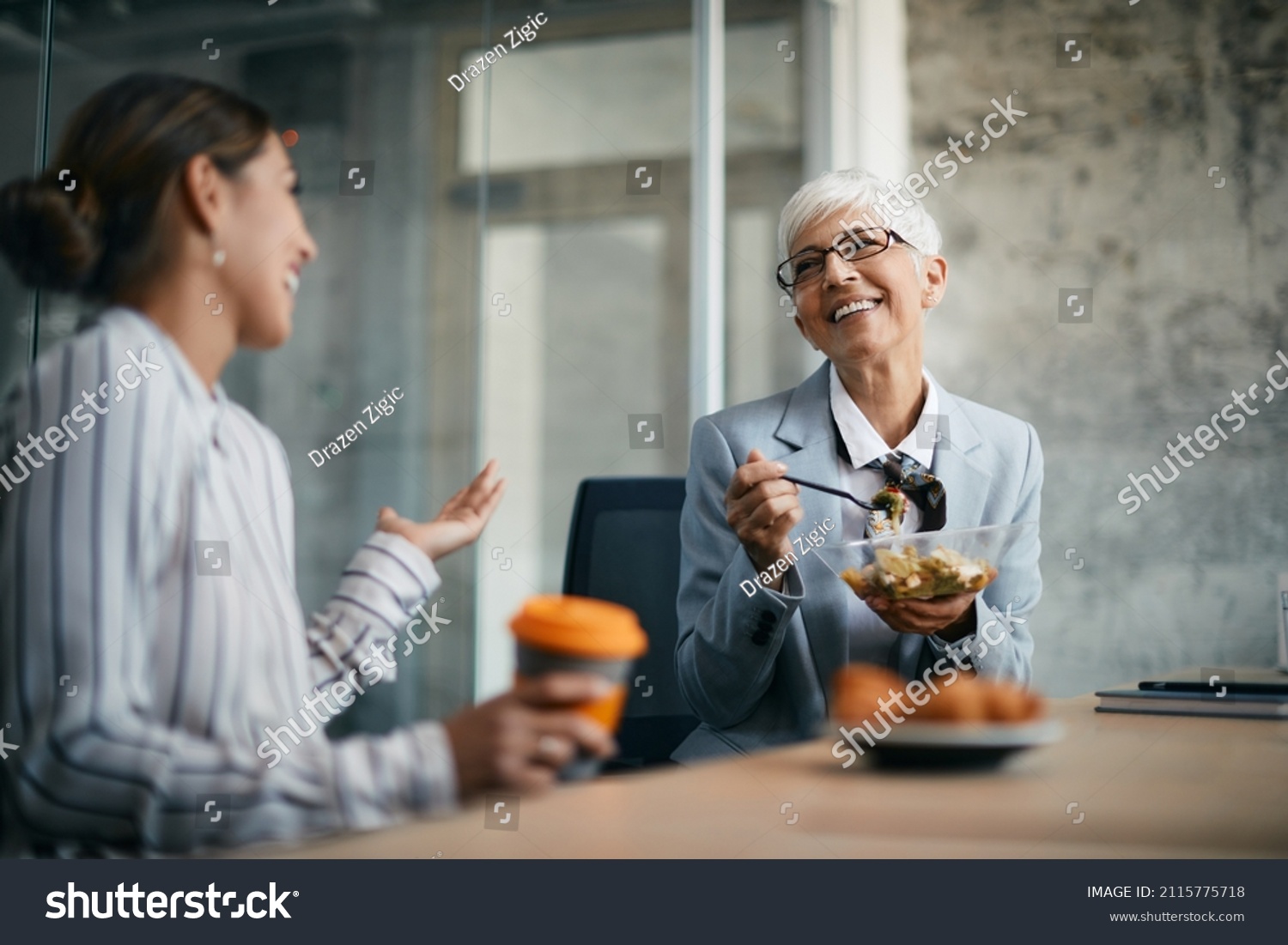 Happy mature businesswoman enjoying in conversation with female coworker during her lunch break in the office. #2115775718