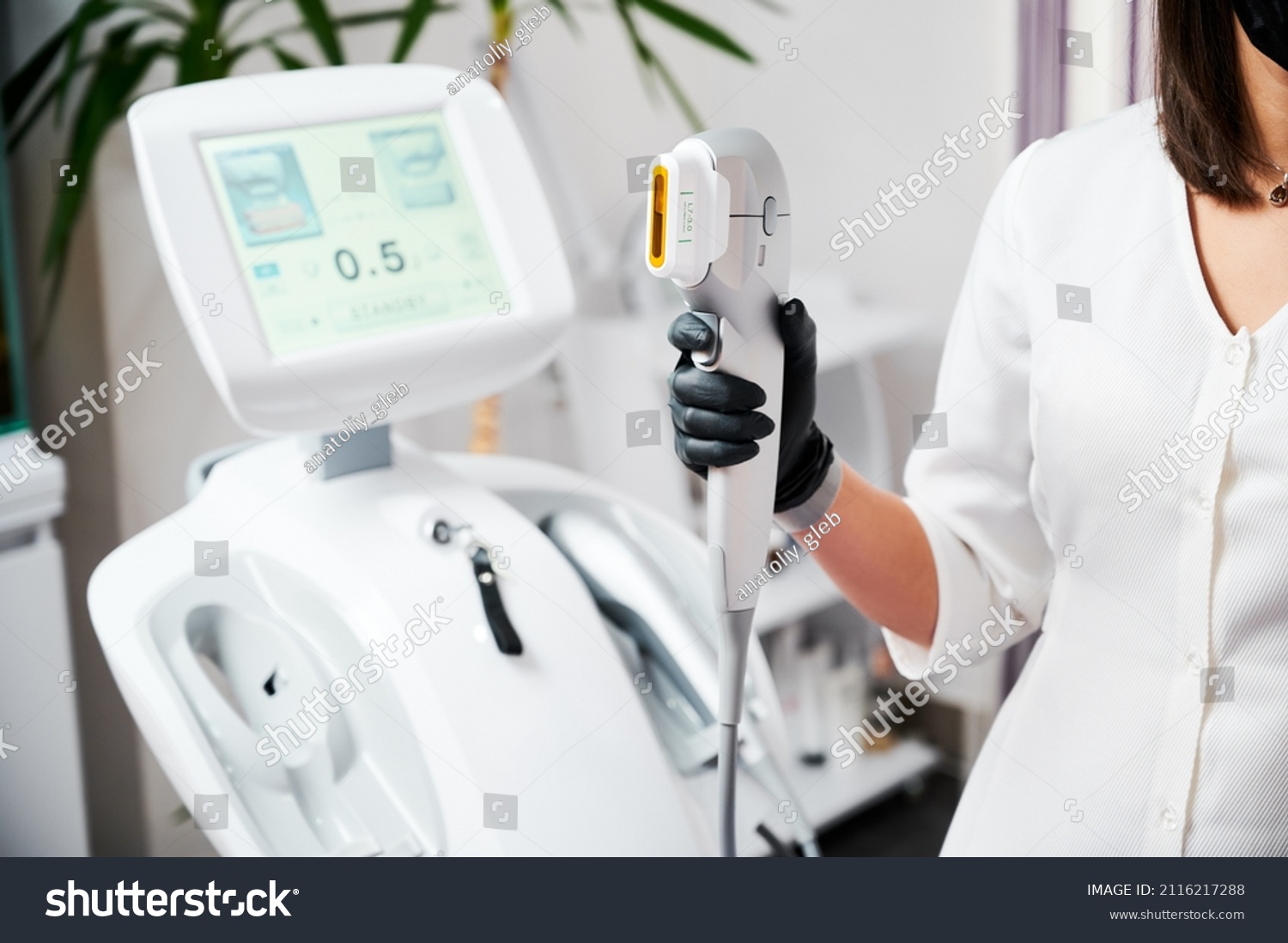 Close up of beautician hand in black glove holding ultrasound device for face lifting and skin tightening procedure. Young woman cosmetologist using modern cosmetology equipment in clinic. #2116217288