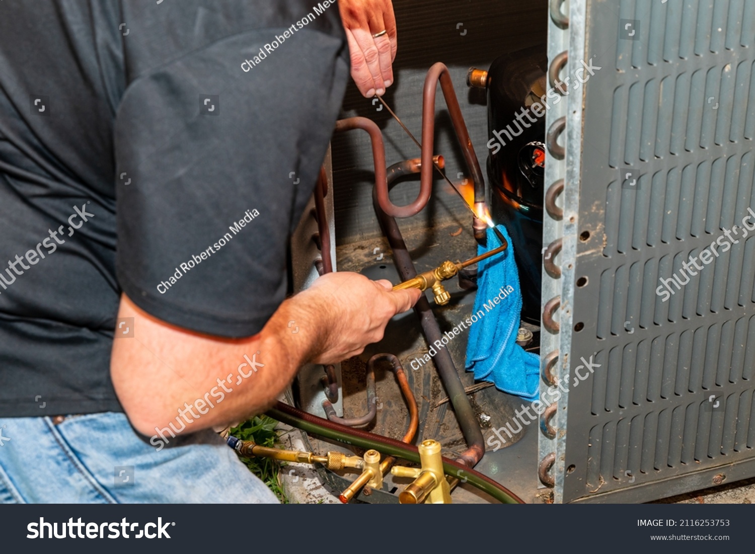 Maintenance worked uses and oxygen Acetylene torch to braze copper tubing on an air conditioner system #2116253753