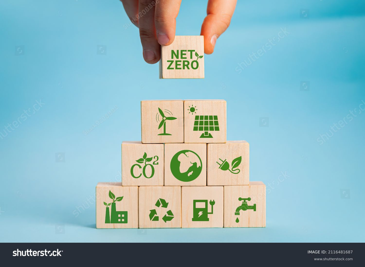 Net zero and carbon neutral concept. Net zero greenhouse gas emissions target. Climate neutral long term strategy. Hand put wooden cubes with green net zero icon and green icon on grey background. #2116481687
