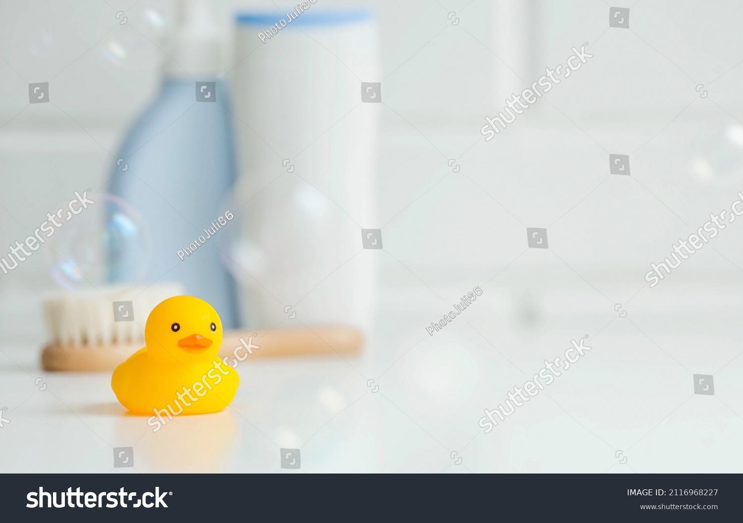 Baby bath accessories. Child care. Miniature yellow rubber duckling for bathing with a brush and shampoo bottles. Soap bubbles, bath foam. #2116968227
