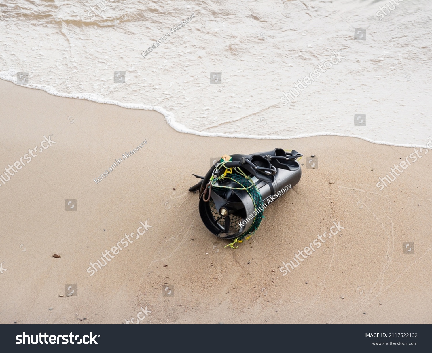 Diver's equipment on sea coast. Rubber flippers and diver propulsion vehicle. Black underwater scooter or swimmer delivery vehicle on sandy beach near sea surf.  #2117522132
