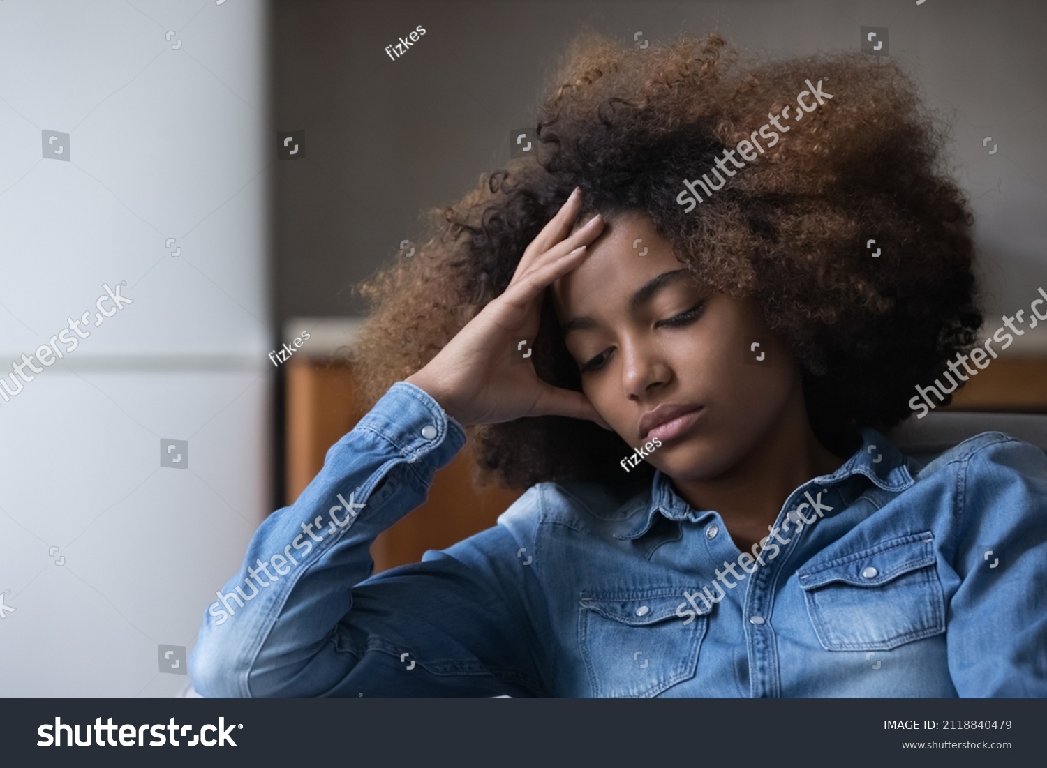Frustrated unhappy African teen girl suffering from depression, melancholy at home, sitting on couch, touching head, feeling bad due to stress, hurt, despair, emotional problems, youth crisis #2118840479
