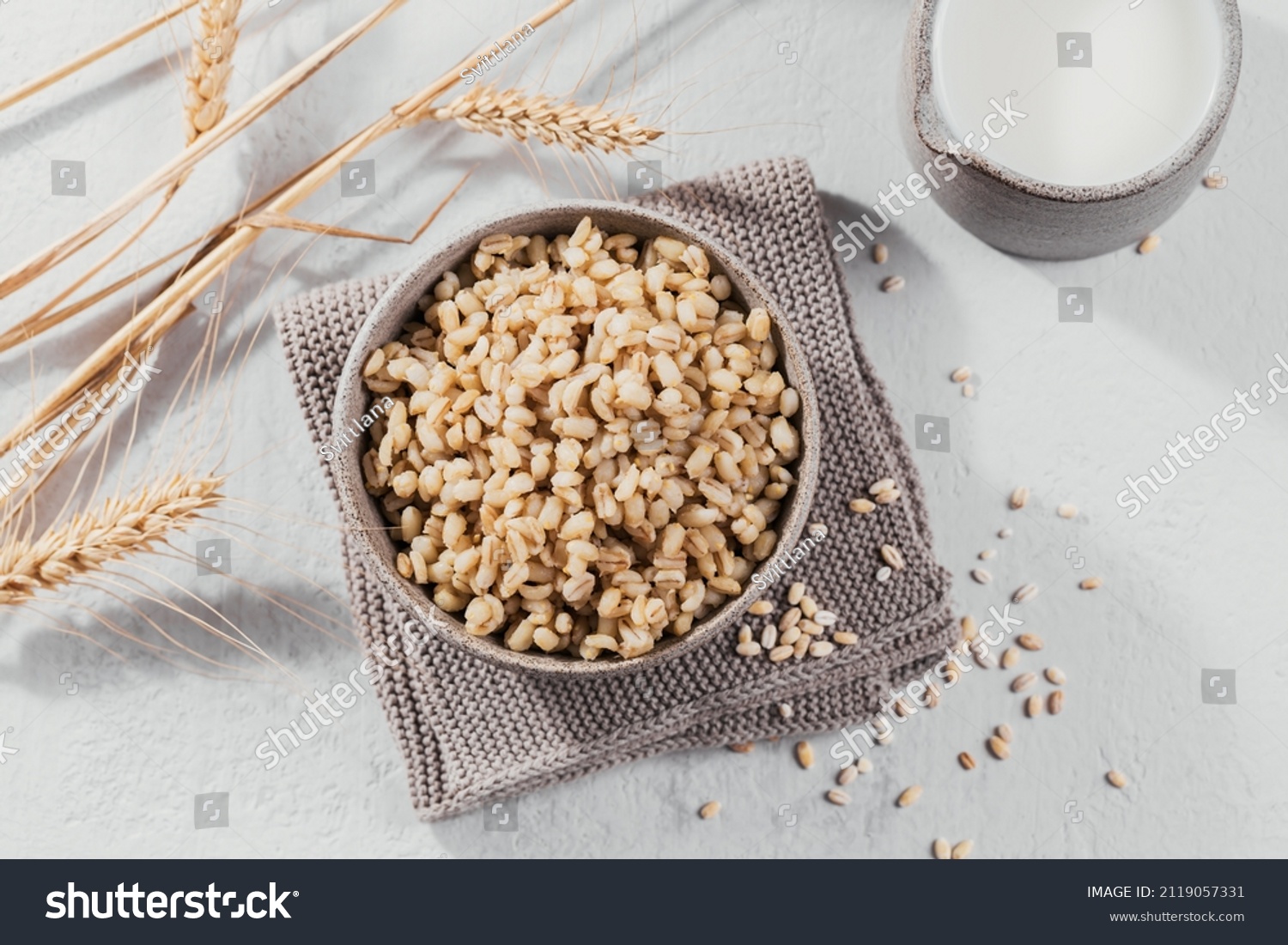 Bowl of cooked peeled barley grains porridge with ears of wheat on light background. Cooking Healthy and diet food concept. #2119057331