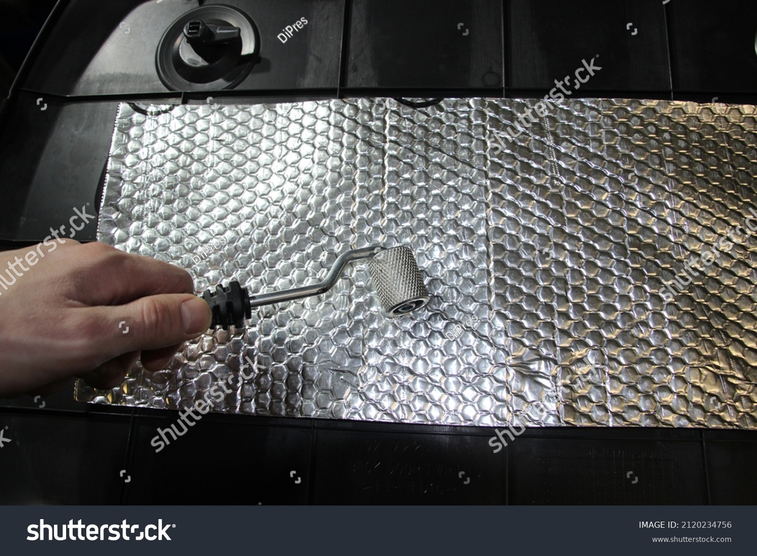 Working hands roll soundproofing material on the car parts.A worker glues sound insulation material onto a plastic part of the car.The process of installing sound insulation of the car.Vibrationdamper #2120234756