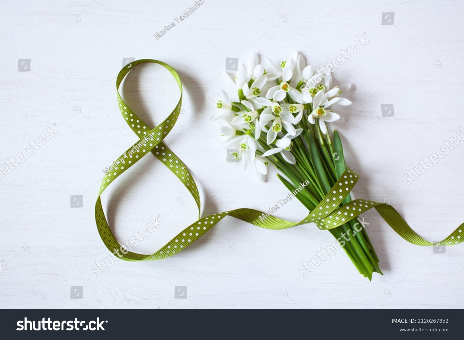 Geeting card for Women's day march 8, number eight from a green ribbon and a bouquet of snowdrops on a white wooden background #2120267852