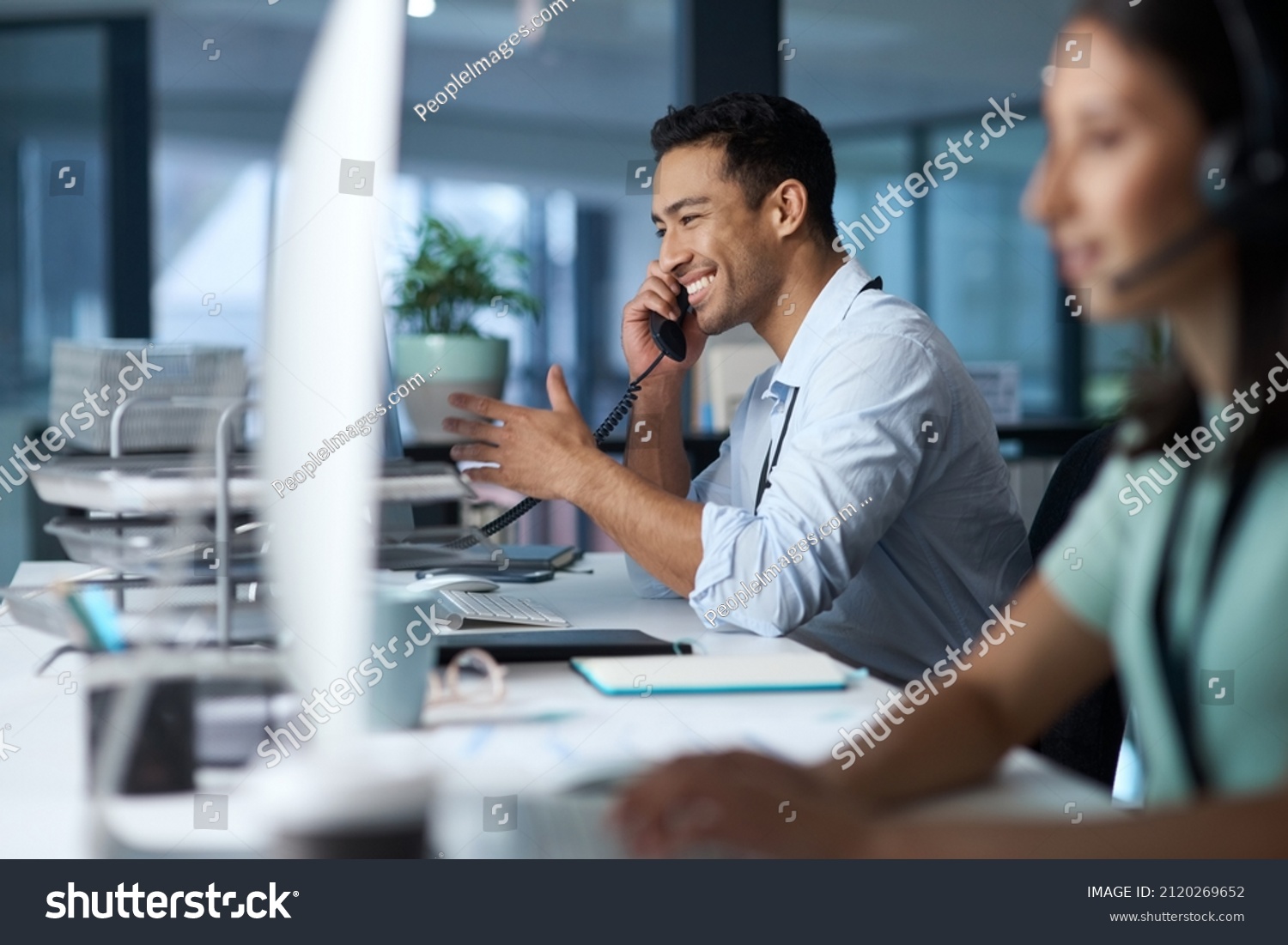 Good business is based on good communication. Shot of a young man answering the phone while working in a modern call centre. #2120269652