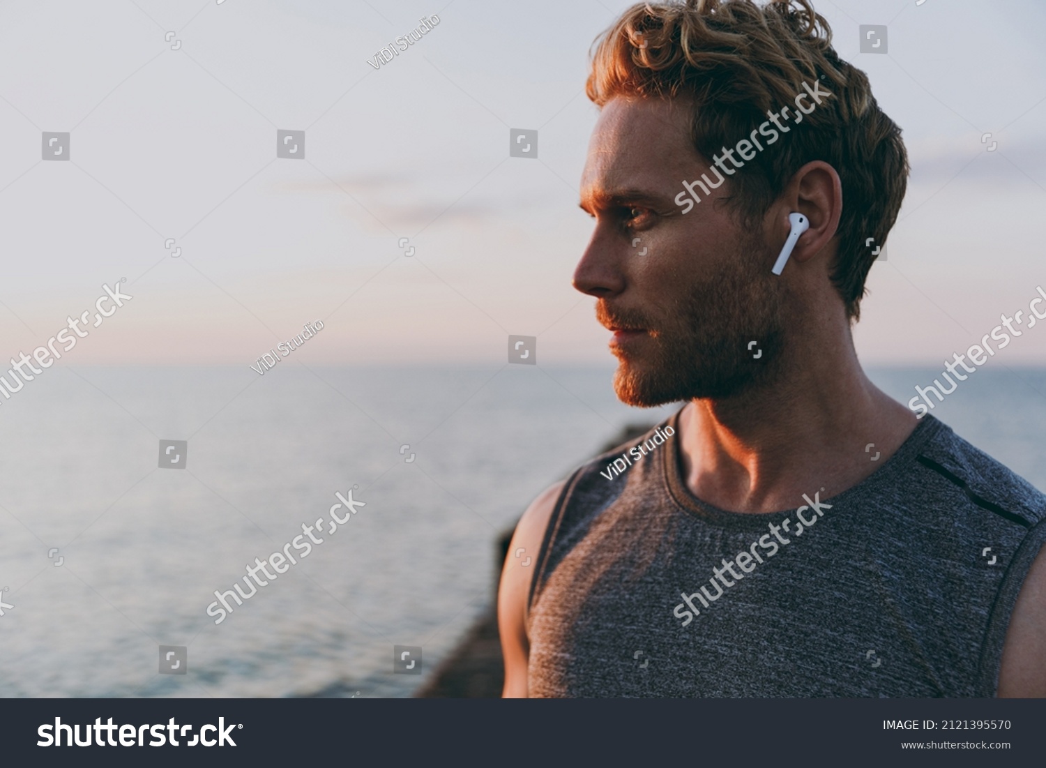 Close up side view young strong athletic toned fit sportsman man in sports clothes earphones warm up train with music at sunrise sun dawn over sea beach outdoor on pier seaside in summer day morning. #2121395570