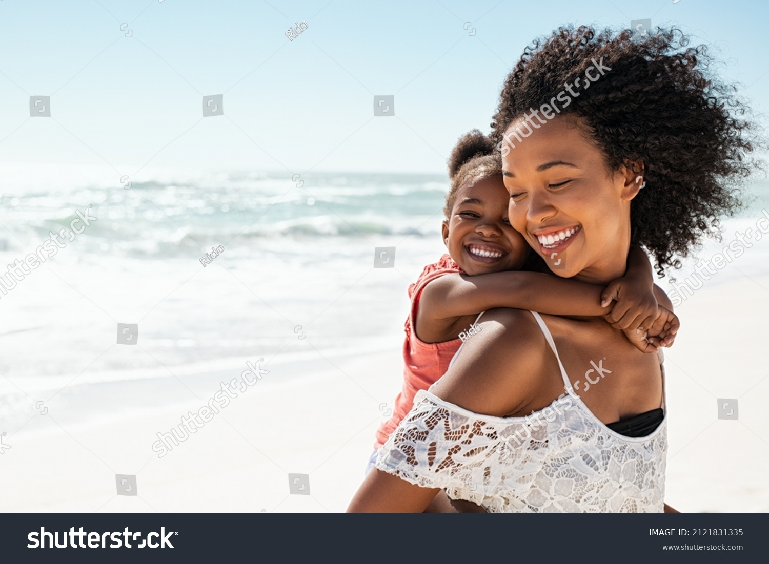 Smiling young black mother and beautiful daughter having fun on the beach with copy space. Portrait of happy sister giving a piggyback ride to cute little girl at seaside. Lovely kid embracing her mom #2121831335
