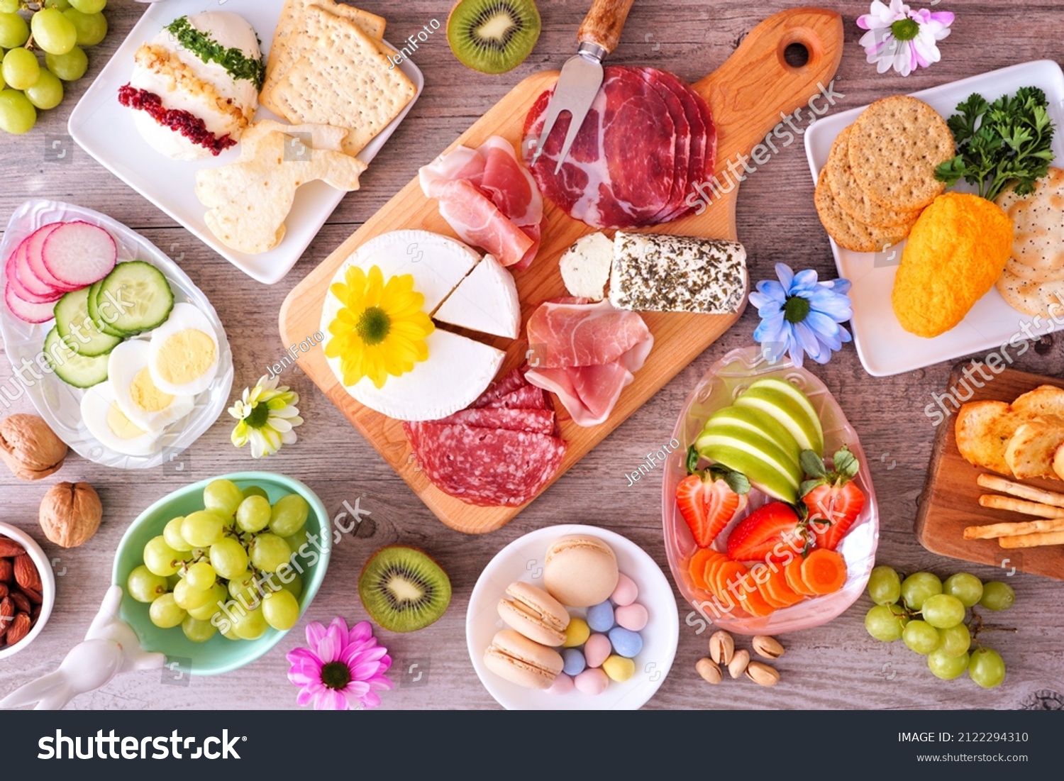 Spring or Easter theme charcuterie table scene against a wood background. Collection of cheese, meat, fruit and vegetable appetizers. Overhead view. #2122294310