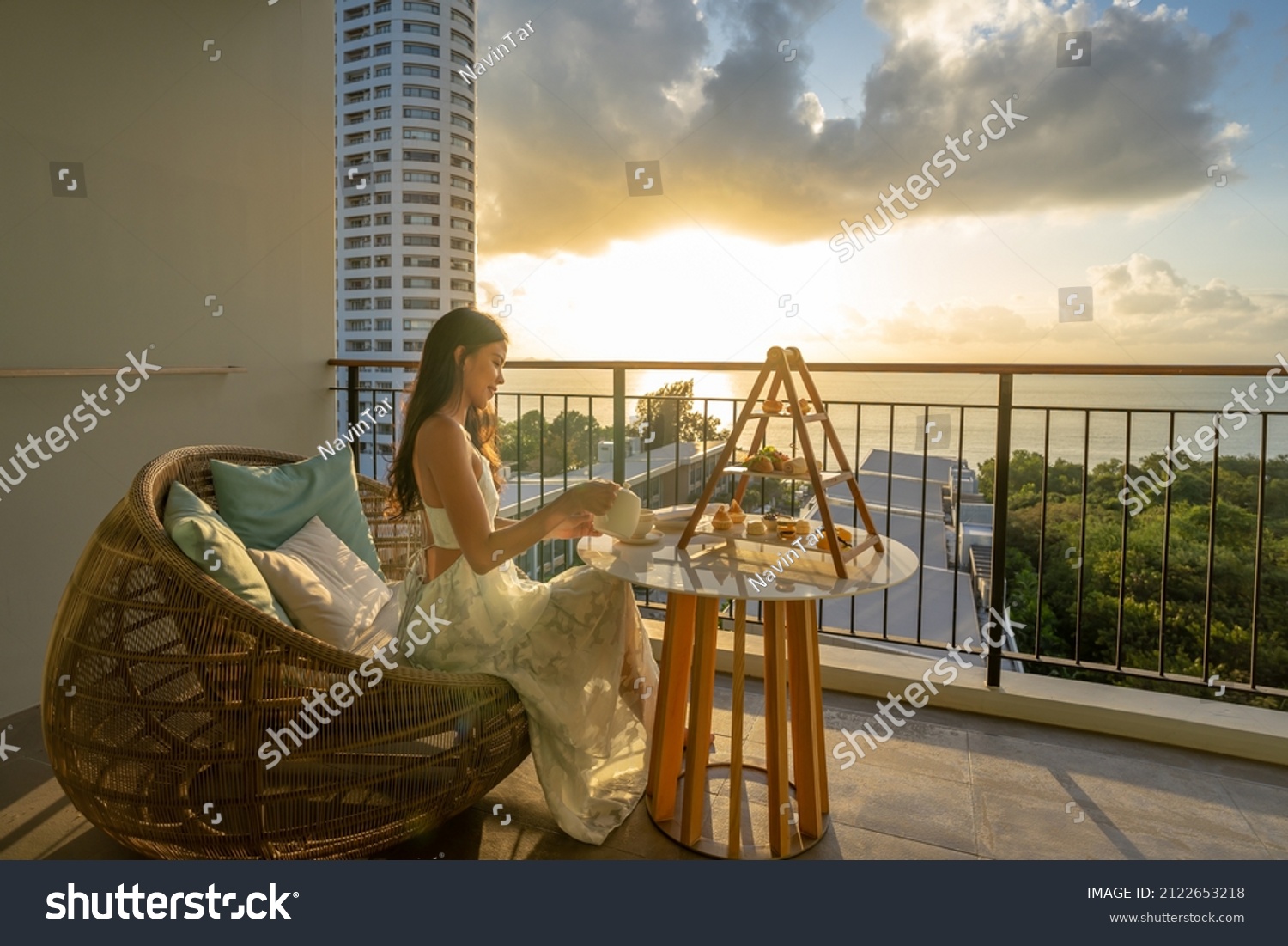 Beautiful asian woman wearing dress enjoying afternoon tea and dessert at balcony on the sunset. #2122653218