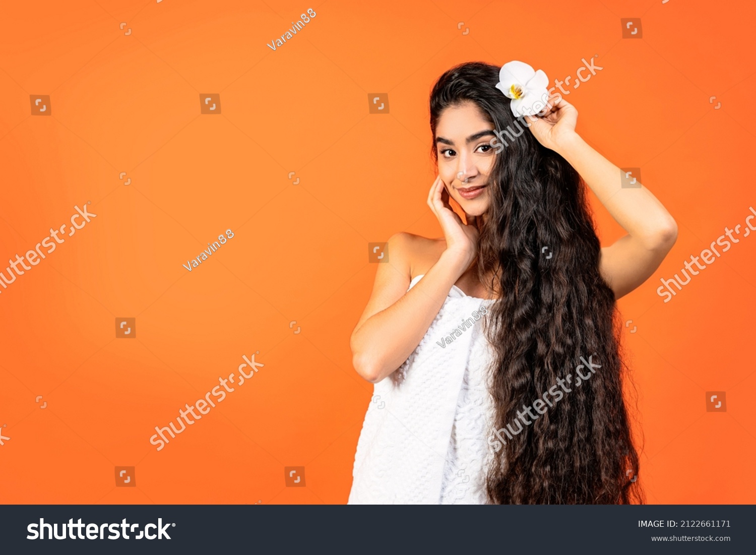 Spa and Wellness background with a beautiful indian woman with healthy long hair. She is dressed in a white towel, her hair is decorated with an orchid and she is looking at us. #2122661171