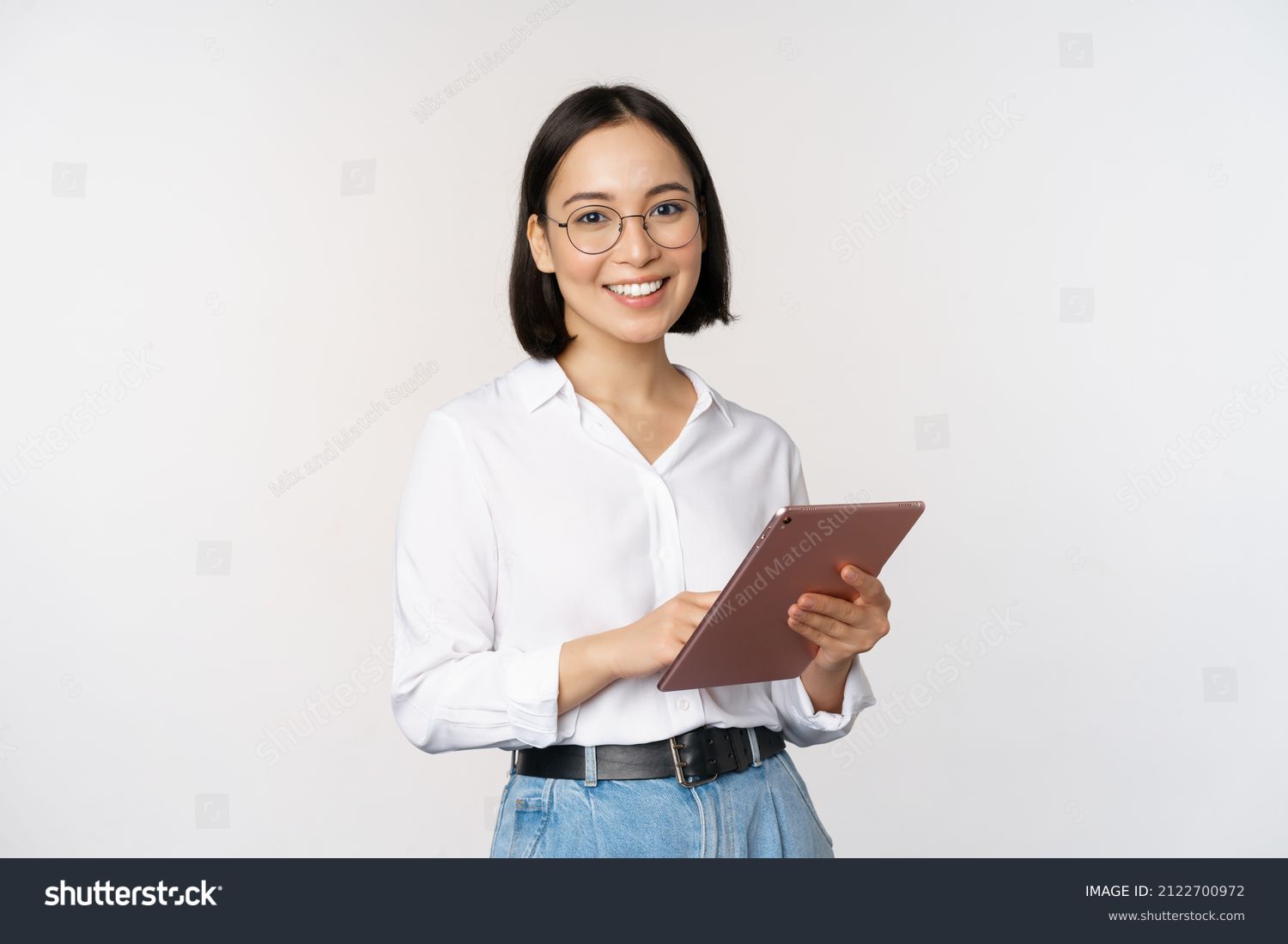 Image of young asian woman, company worker in glasses, smiling and holding digital tablet, standing over white background #2122700972