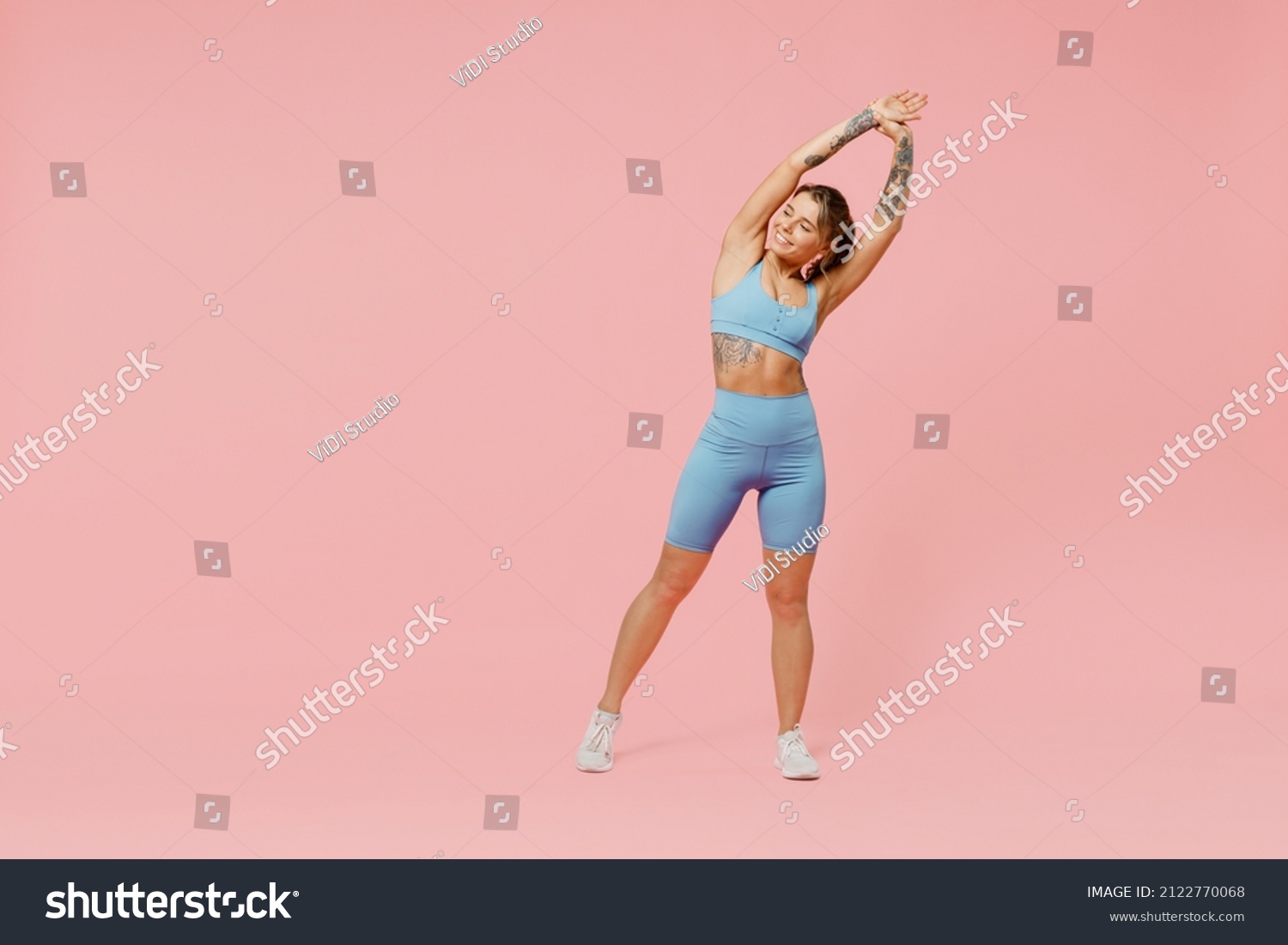Full body young sporty fitness trainer woman wear blue tracksuit spend time in home gym tilt body to sides with hand stretch lunge exercise isolated on plain pink background. Workout sport concept. #2122770068