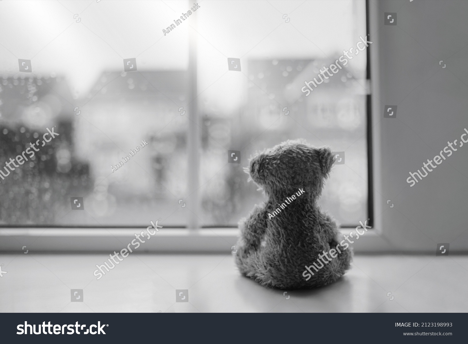 Black and white Rear view Lonely bear doll sitting alone looking out of window, Sad teddy bear sitting next to window in rainy day, lost toy, Loneliness concept, International missing Children day #2123198993