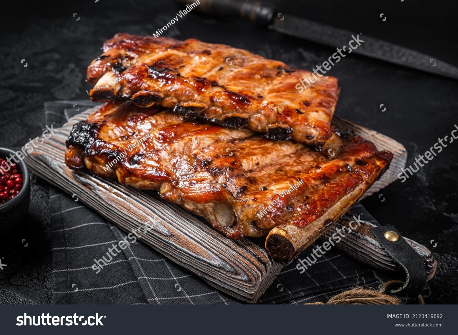 Stack of grilled pork ribs in BBQ sauce on a chopping board. Black background. Top view #2123419892