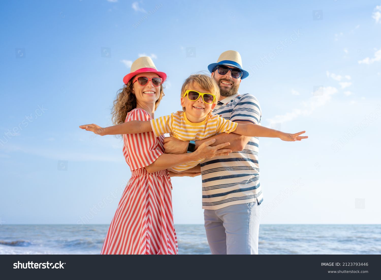 Happy family having fun on the beach. Mother and father holding son against blue sea and sky background. Summer vacation concept #2123793446