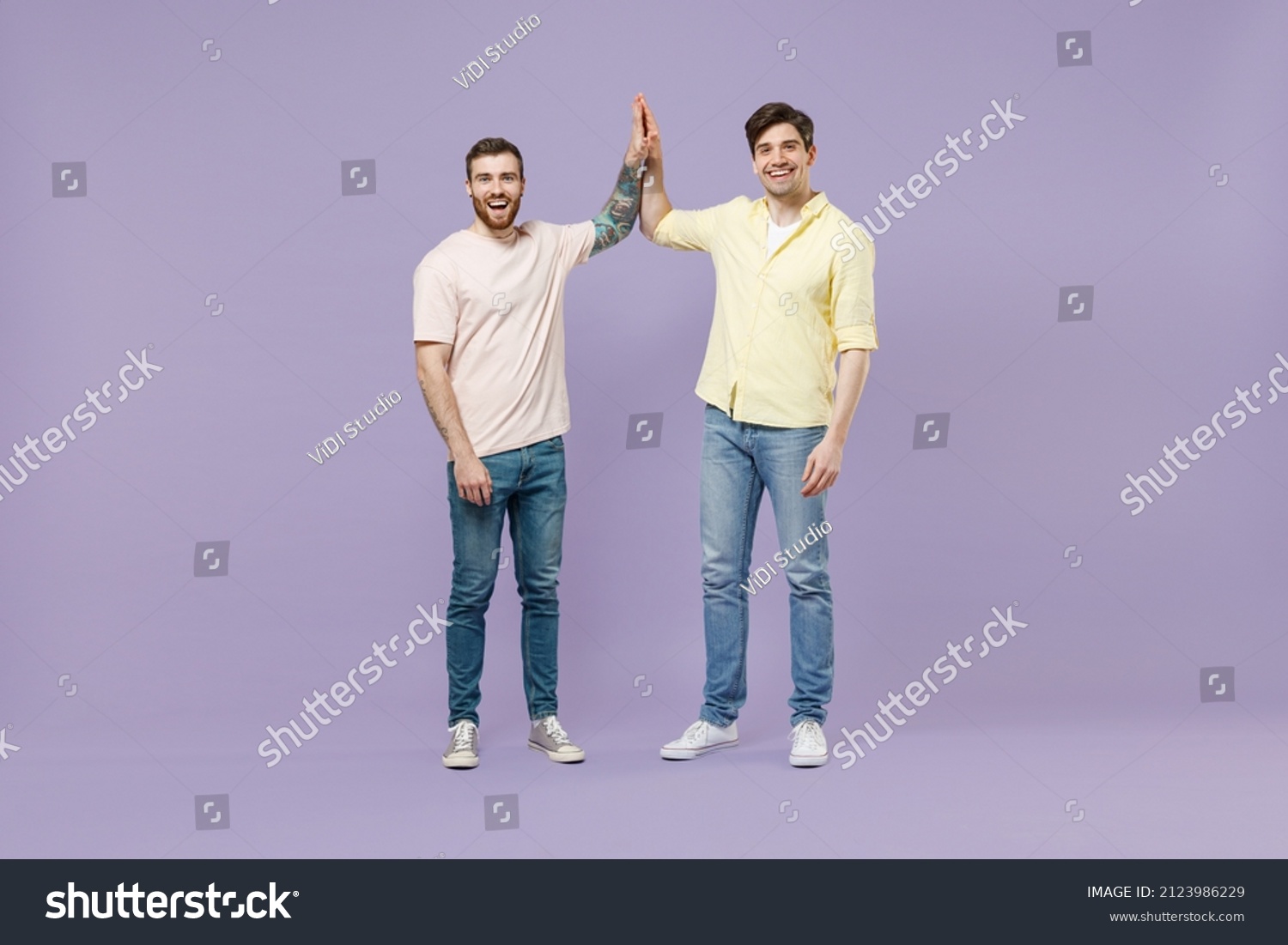 Full size length two young smiling happy men friends together in casual t-shirt meeting together greeting give high five clapping hands folded isolated on purple background studio Tattoo translate fun #2123986229