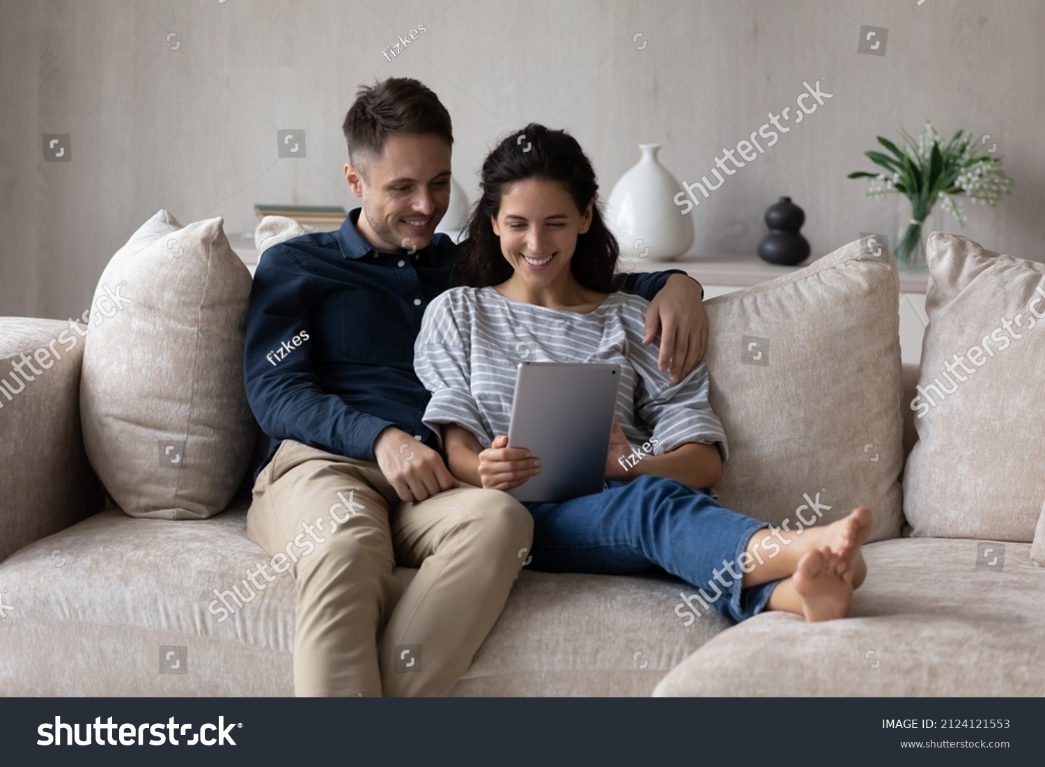 Millennial husband and wife using online application on tablet, watching media content, movie, talking on video call together. Happy couple holding digital gadget, relaxing on cozy couch at home, #2124121553