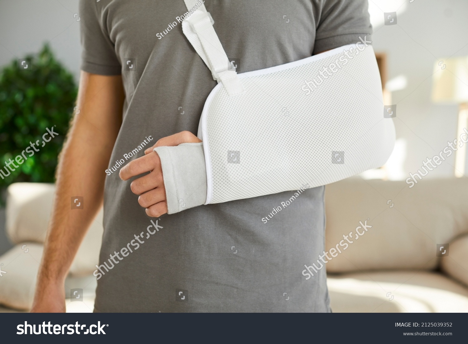 Close up of sling on broken arm of man he needs to wear during rehabilitation period. Unknown male patient wearing immobilizer after car accident or after sports injury. Orthopedics concept. #2125039352