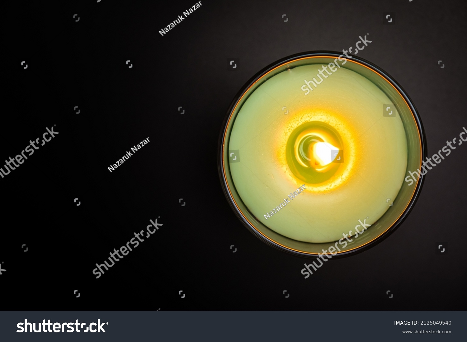 Burning aroma candle in glass on black background top view. Green aromatic wax candle with copy space. Candlelight close up #2125049540