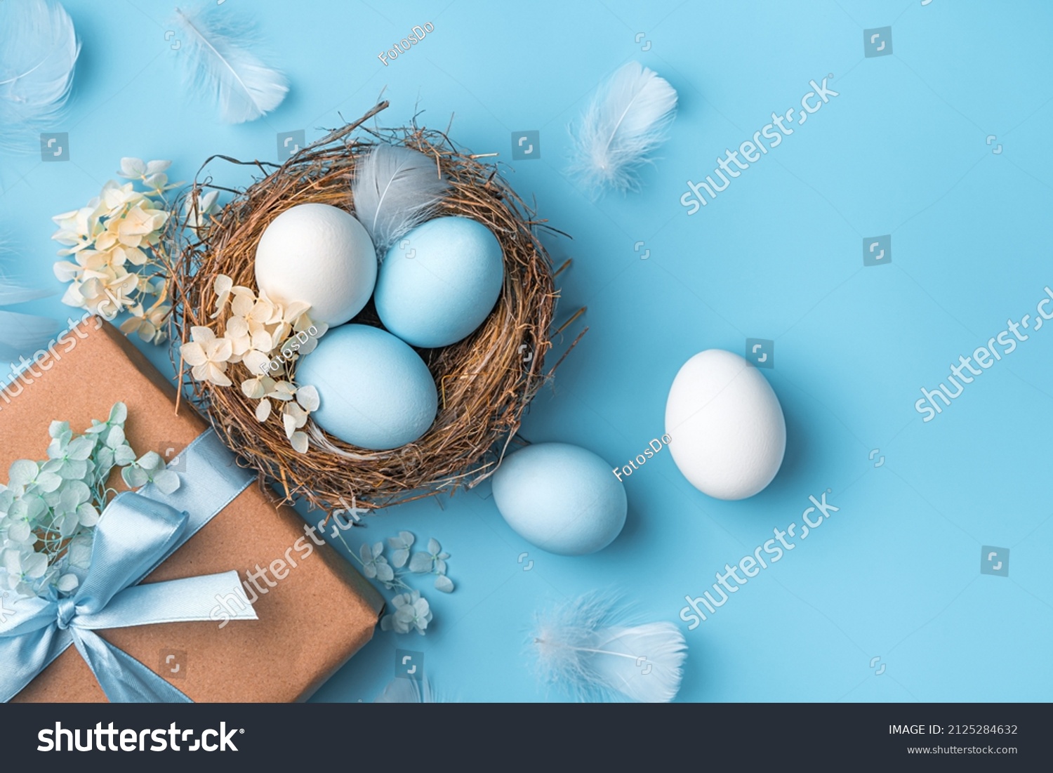 Easter pastel background with eggs, a nest and a gift on a blue background. The concept of a Happy Easter. Top view, copy space. #2125284632