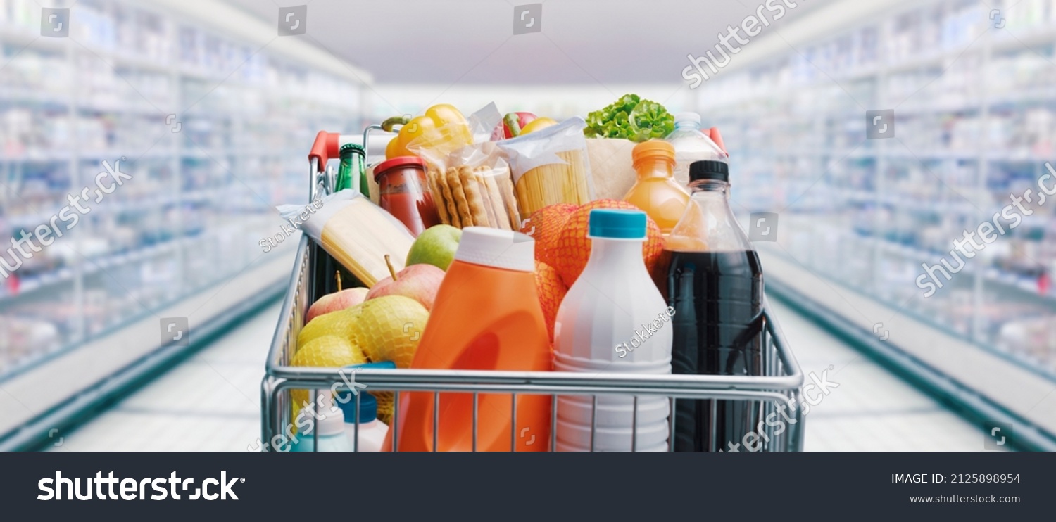 Shopping cart filled with food and drinks and supermarket shelves in the background, grocery shopping concept #2125898954