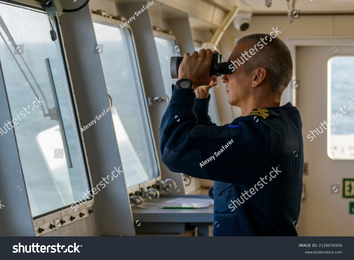 Deck officer with binoculars on navigational bridge. Seaman on board of vessel. Commercial shipping. Passenger ship. #2126076956