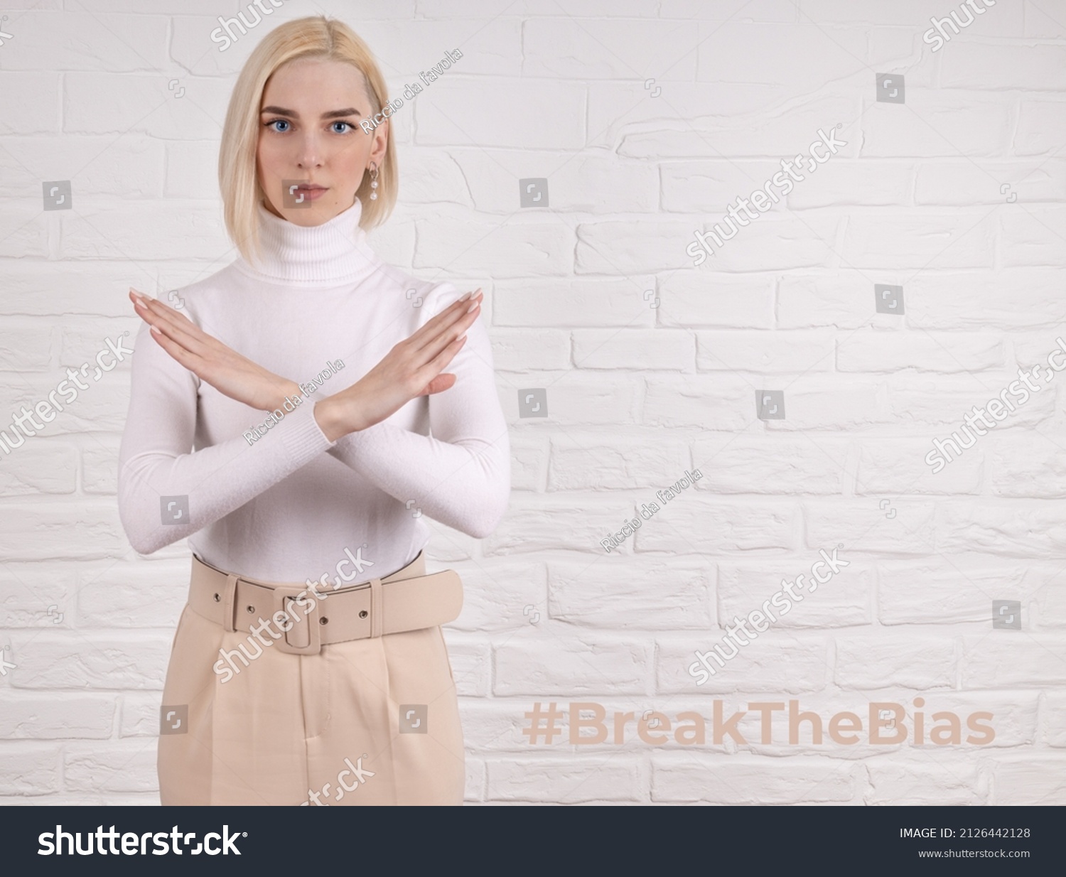 Break the bias symbol of woman's international day. The arms of a girl in white are crossed on a white brick wall. Woman arms crossed to show solidarity, breaking stereotypes, inequality
 #2126442128