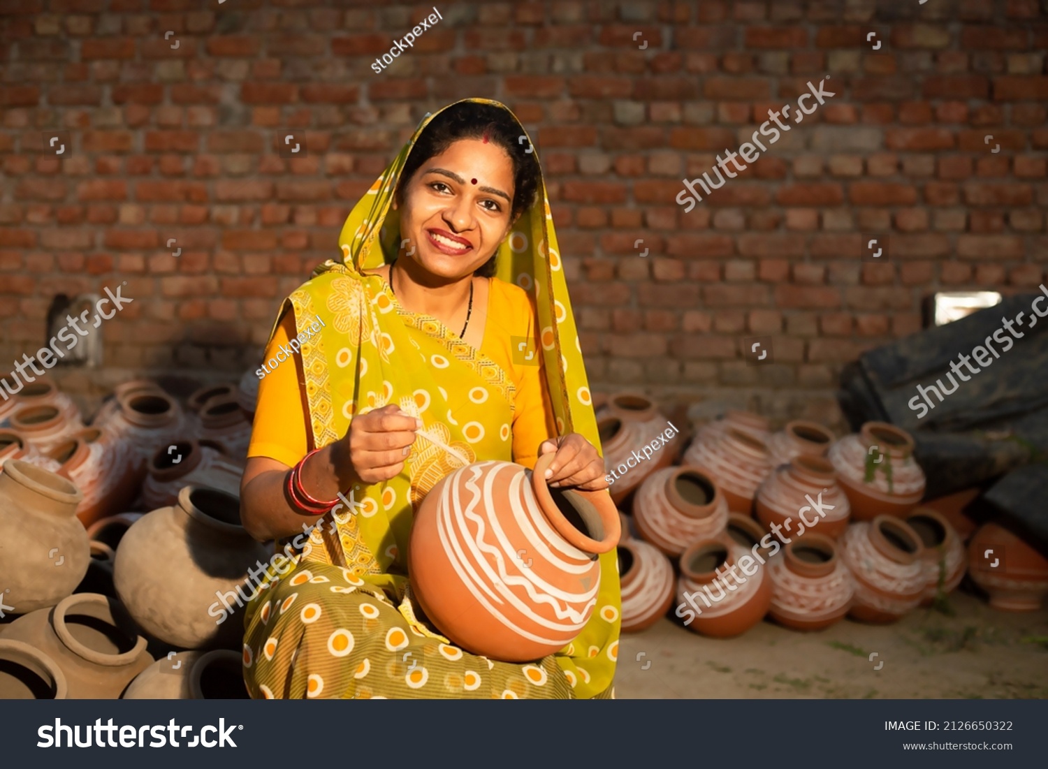 Portrait of happy traditional Indian woman potter artist painting and decorating design on clay pot for sale, handicraft, skill india. #2126650322