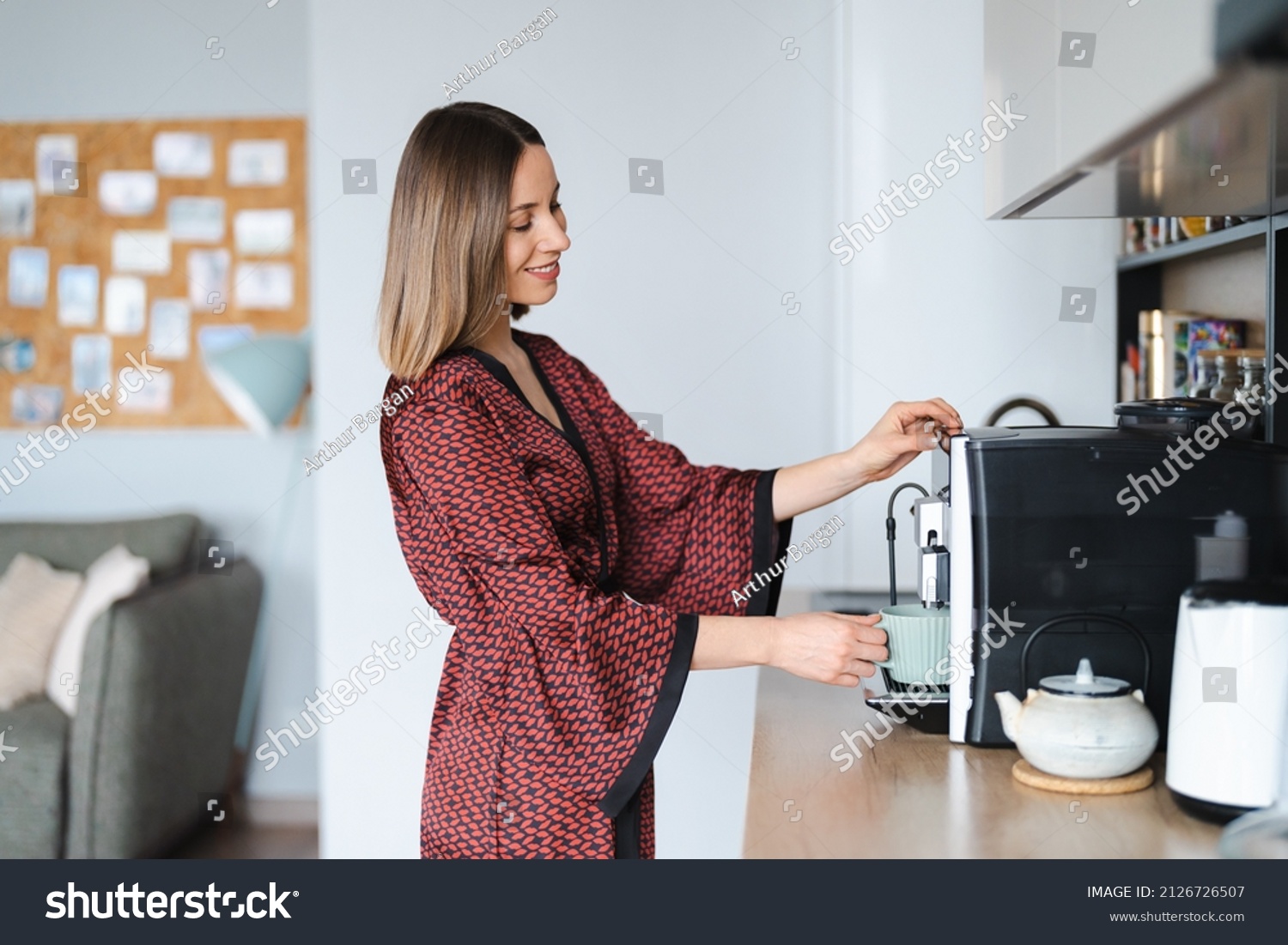 Woman using coffee machine to make big mug of coffee at home. Woman wearing silk robe at home while preparing a latte #2126726507