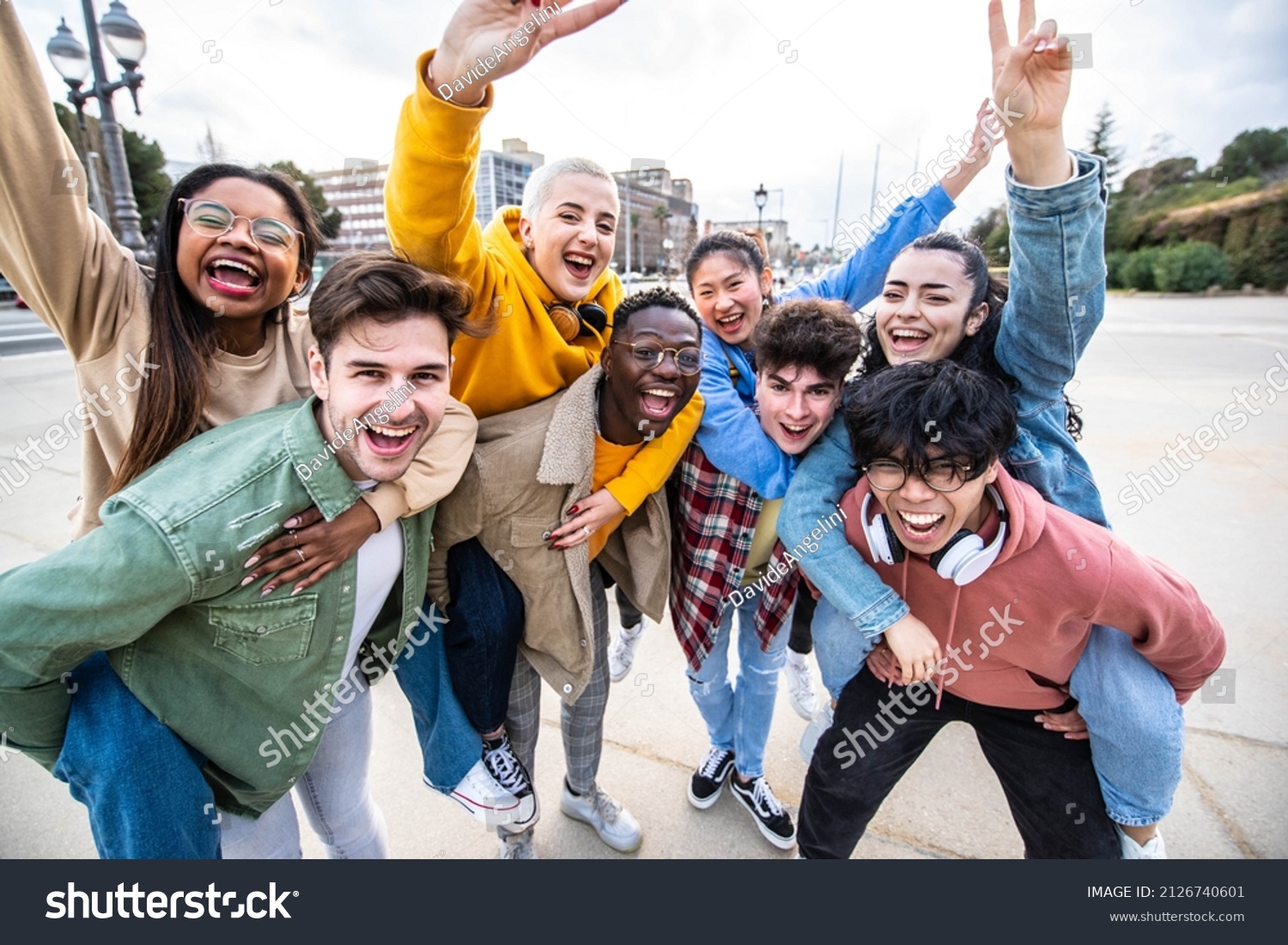 Group of young people with hands up looking at camera - Millenial friends having fun together on city street - Multicultural students walking outside university campus - Youth culture and scholarship #2126740601