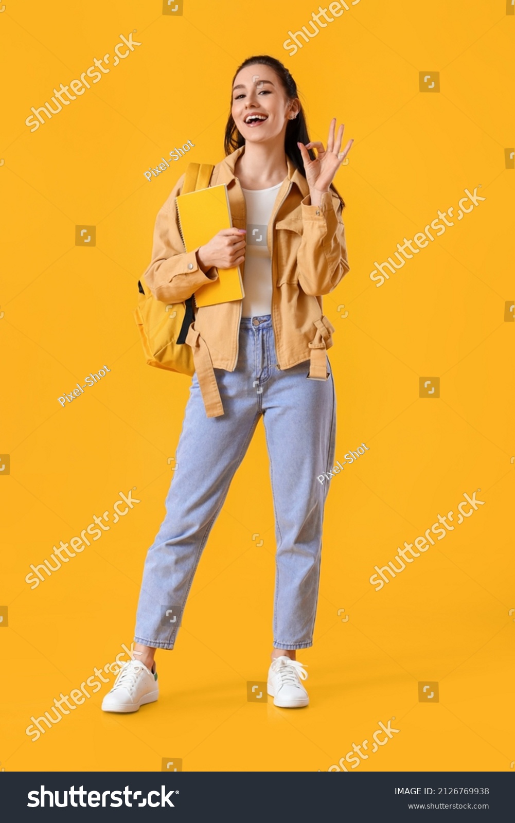 Portrait of beautiful female student showing OK gesture on color background #2126769938
