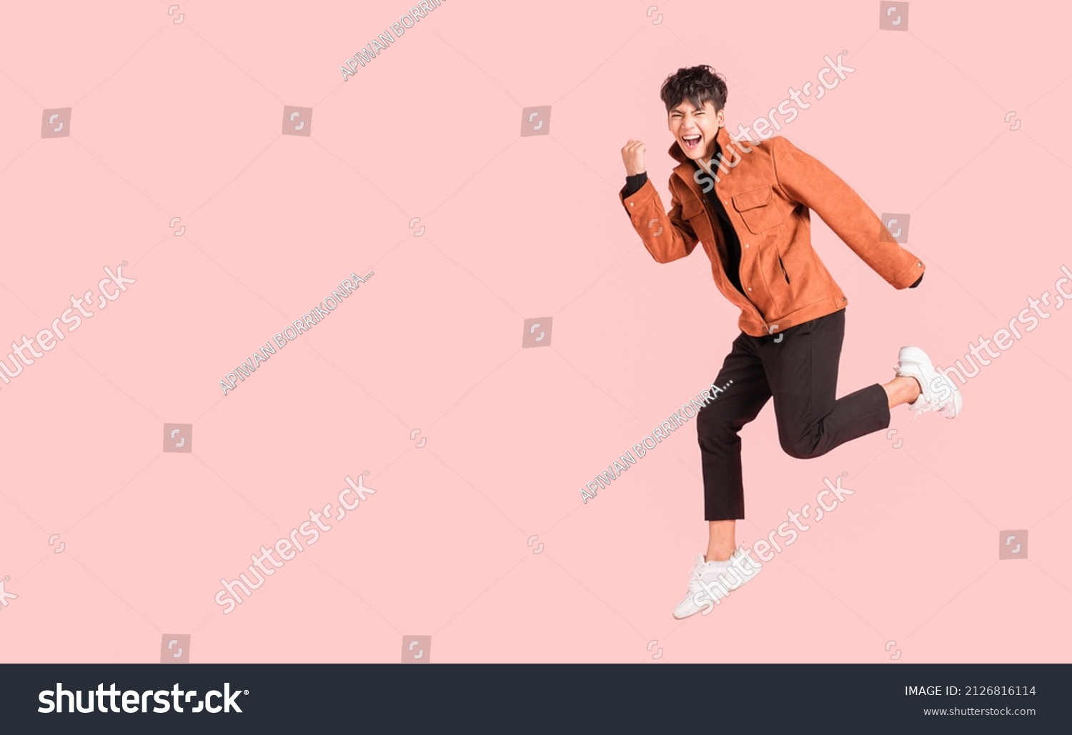 Happy handsome Asian man in fashionable clothing and jumping doing winner gesture isolated on pink background. Portrait of young male cheerful confident and excited jump in air and smile in studio. #2126816114
